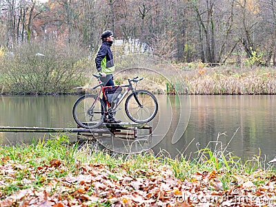 Cyclist stay at his trekking bike on small pond pier and watching swans Stock Photo