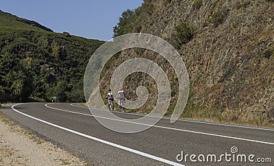 Cyclists biking in a curved empty spanish road during the summer, Triacastela, Galicia, Spain. Editorial Stock Photo