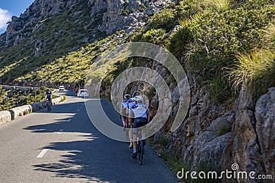 Cyclists cycling in shade on country road by mountain during sunny day Editorial Stock Photo