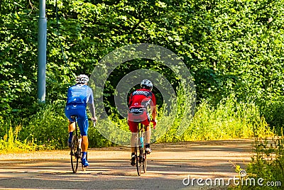 Cyclists train on a forest road with sports bikes. Athletic men in helmets ride a bicycle on the road. Back view on professional Editorial Stock Photo