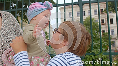 Little girl in mother arms looks teenage boy, getting acquainted with new face. Editorial Stock Photo