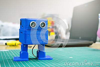 3D printed Funny blue robot on the background of devices and laptop. Robot model printed on automatic three dimensional 3d Stock Photo