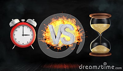 3d rendering a large flaming word VS stands between a red retro alarm clock and a hourglass. Stock Photo