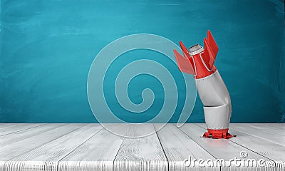 3d rendering of a red and silver realistic model of a retro rocket stands crashed into a wooden desk on a blue Stock Photo