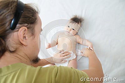 Dad changing diaper on baby girl on bed, changing nappy, everyday care Stock Photo