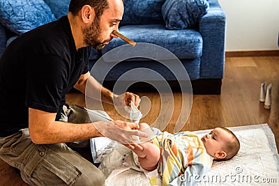 Dad cleaning his baby`s dirty ass, changing the stinky diaper with a nose clip, fatherhood and humor Stock Photo