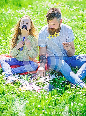 Dad and daughter sits on grass at grassplot, green background. Child and father posing with eyeglases and muastache Stock Photo