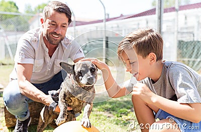 Dad and his son taking care of abandoned dog in animal shelter Stock Photo