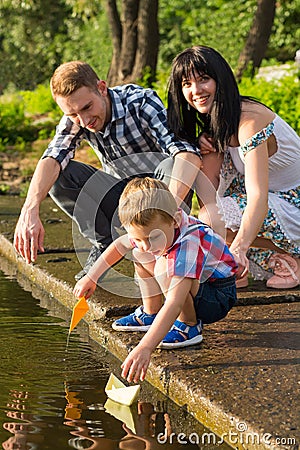 Mom, dad and their little son launch paper boats in a river in t Stock Photo