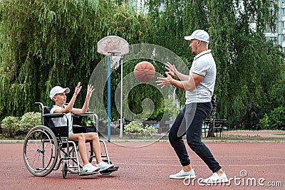 Dad plays with his disabled son on the sports ground. Concept wheelchair, disabled person, fulfilling life, father and son, Stock Photo