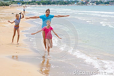 Dad with two children running merrily along the seashore Stock Photo