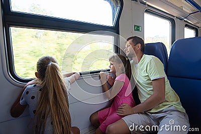 Dad and two daughters in an electric train car, look out the window with enthusiasm Stock Photo