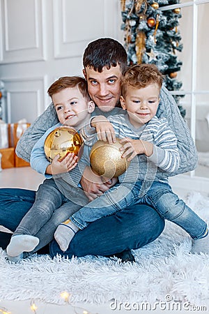 A a daddy with his two sons twins in front of the christmas tree hugging and having fun. big family concept Stock Photo