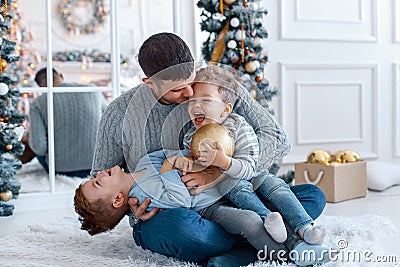 A a daddy with his two sons twins in front of the christmas tree hugging and having fun. big family concept Stock Photo