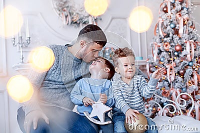 A a daddy with his two sons twins in front of the christmas tree hugging and having fun. big family concept Stock Photo