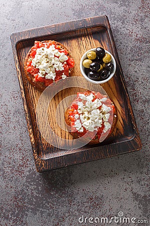Dakos Cretan Meze appetizer with barley rusk, tomatoes, feta cheese, oregano and olive oil closeup on the wooden board. Vertical Stock Photo