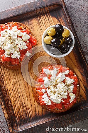 Dakos or Ntakos traditional Greek starter made of dried bread with tomato feta, oregano and olive oil closeup on the wooden board Stock Photo