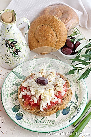 Dakos traditional Greek appetizer on a traditional plate with ceramic olive oil jar, dry rye bread, olives and olive branch. Stock Photo