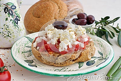 Dakos traditional greek appetizer on a traditional plate with ceramic olive oil jar, dry rye bread, olives and olive branch. Stock Photo
