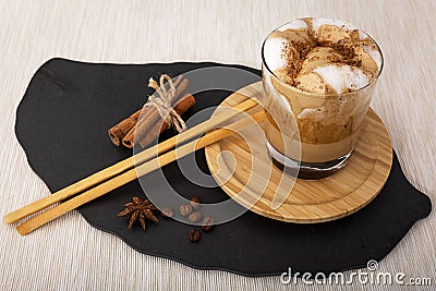 Dalgon coffee in a glass Cup on a wooden saucer next to breadsticks, cinnamon, coffee beans and a bucket Stock Photo