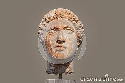 Damaged head of ancient Greek statue with part of face rough and orange from deterioration isolated against tan background Stock Photo