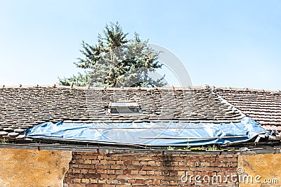 Damaged roof with tiles on the old house covered with plastic nylon to protect interior from rain water Stock Photo