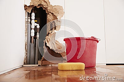Damaged wall, exposed burst water pipes, sponge and bucket Stock Photo