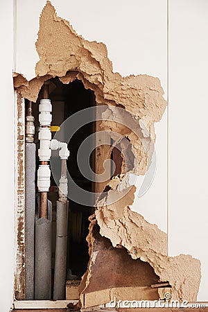 Damaged wall exposing burst water pipes after flood, vertical Stock Photo