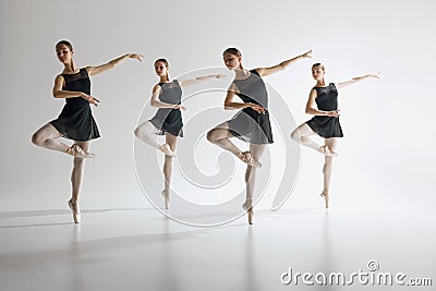 Dance in harmony. Beautiful teen girls, ballerinas in black leotards and pointe in motion, dancing against gray studio Stock Photo