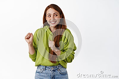 Dancing teen girl with red hair, smiling and looking at upper right corner logo, having fun and partying, standing in Stock Photo