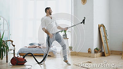 Young man having fun cleaning house with vacuum cleaner dancing like guitarist Stock Photo