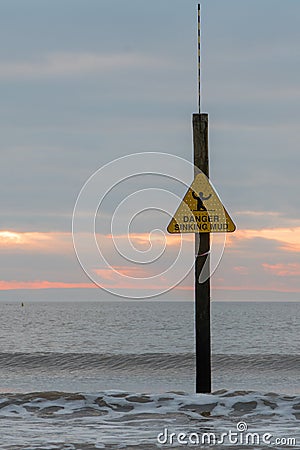 Danger Sinking Mud sign in front of waves and sunset Stock Photo