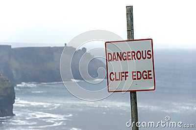 Dangerous cliff edge sign in overcast weather at Cliffs of Moher in Ireland. Danger sign warning. Stock Photo