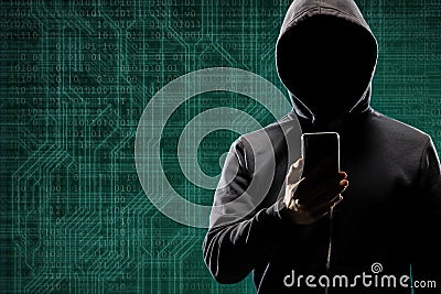 Dangerous hacker with a smartphone gadget over digital background with binary code. Obscured dark face in mask and hood Stock Photo