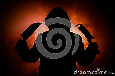 A dangerous hooded man standing in the dark and holding a knife. Face can not be seen. Committing a crime concept. Selective focus Stock Photo