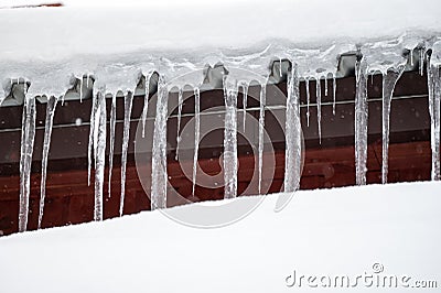 Dangerous sharp icicles and snow hanging from the roof Stock Photo