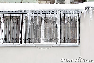 Dangerously hanging icicles from the roof over the window with a fence in winter. Stock Photo