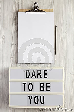 `Dare to be you` on a lightbox, cliboard with blank sheet of paper on a white wooden surface, top view. Flat lay, overhead, from Stock Photo