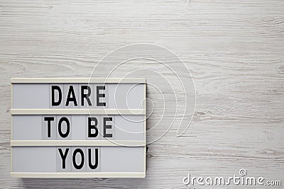 `Dare to be you` on a lightbox, cliboard with blank sheet of paper on a white wooden surface, top view. Flat lay, overhead, from Stock Photo