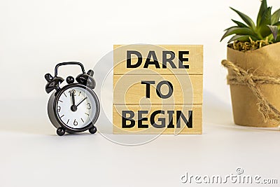 Dare to begin symbol. Wooden blocks with words `Dare to begin`. Beautiful white background, black alarm clock, house plant. Stock Photo