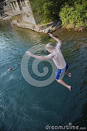 Daring young boy jumping off a bridge into the river. Being adventurous and brave, diving right into the water Stock Photo