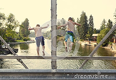 Daring young boys jumping off a bridge into the river. View from behind. Stock Photo