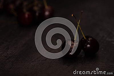 Dark atmospheric image of two ripe red cherries with crossed stems and a pile of cherries in the background on a dark metalic Stock Photo