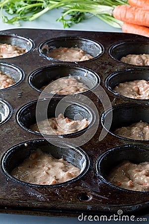 A dark baking muffin tin filled with carrot cake muffin batter. Stock Photo