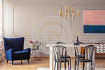 Dark blue armchair in a dining room interior with a table, chairs and golden lamp Stock Photo