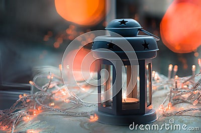 Dark blue and gray candle lantern with blurred orange Christmas lights and bokeh Stock Photo