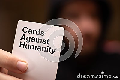Dark blurred out of focus man in the background holding a white cards against humanity card. Adult party game popular worldwide Editorial Stock Photo