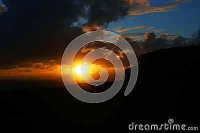 Dark bright sunset with clouds, silhouette of a rock, voluminous clouds Stock Photo