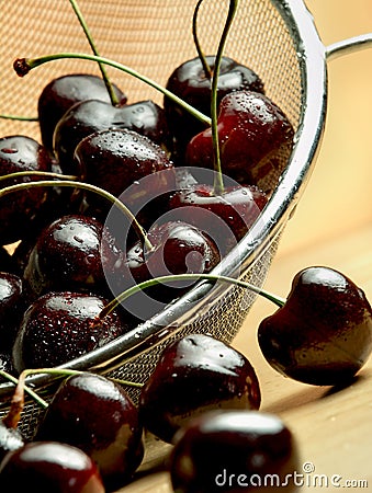 Dark cherries in mesh sieve on wooden table Stock Photo