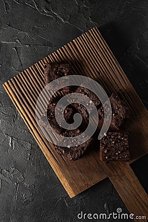 Dark chocolate brownies with choco drops on oak wood cutboard on dark background Stock Photo